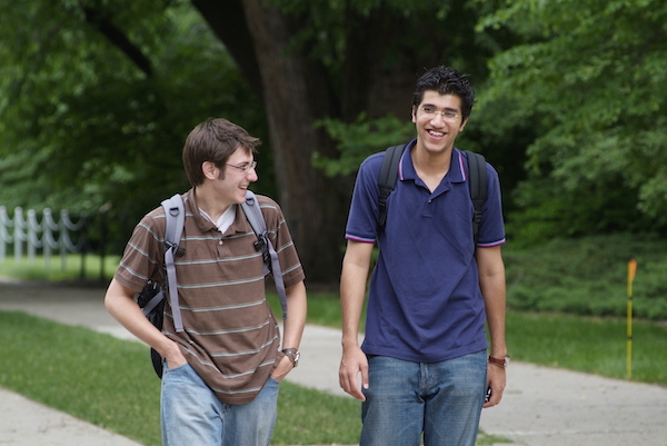 Two students laughing while walking on the sidewalk