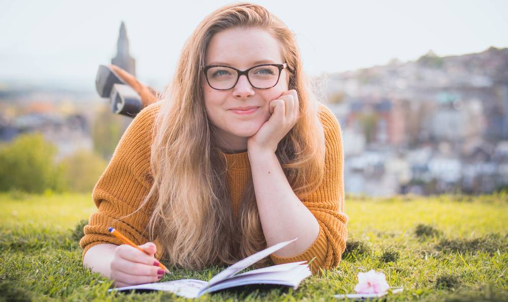 woman lying on grass writing in notebook